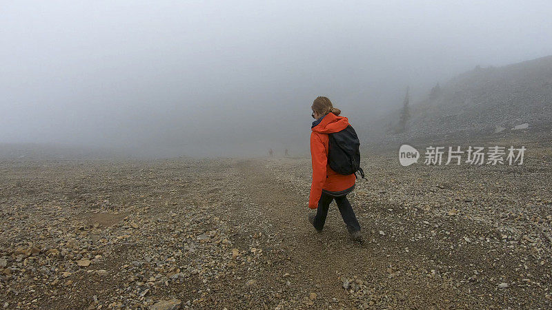 年轻的女登山运动员在雾中爬下一座山