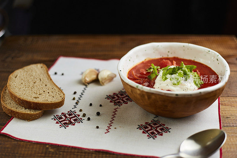 木桌上手工陶碗里的罗宋汤配酸奶油。包括面包，青葱，辣椒和大蒜。传统的乌克兰菜。