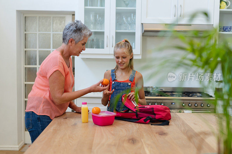 年长的白人祖母在厨房给孙女准备午餐和水果