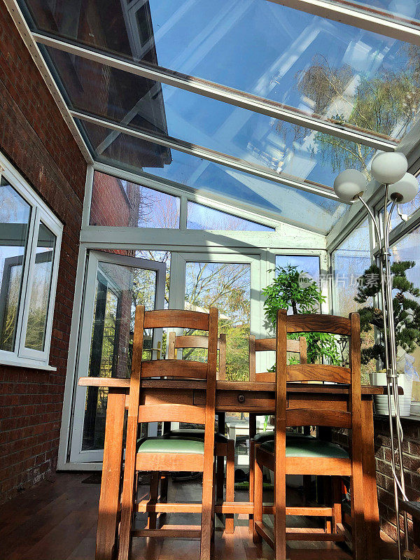 室内的玻璃温室，用餐区，深色木质餐桌和椅子，敞开的门可以看到家庭花园