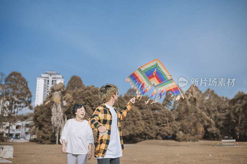 一个亚洲华人少年和他的祖母在一个阳光明媚的早晨在公园里玩风筝