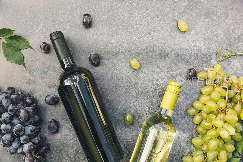 瓶身红色和白色的葡萄酒，绿色的藤蔓，葡萄酒杯和成熟的葡萄在古老的黑石桌背景。葡萄酒店、酒吧、酒庄或葡萄酒品尝概念