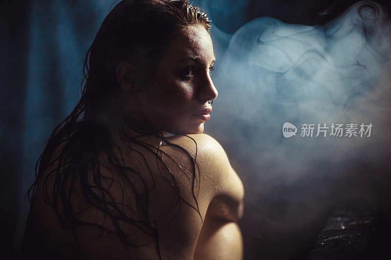 一个湿漉漉的女人坐在昏暗潮湿的浴室里