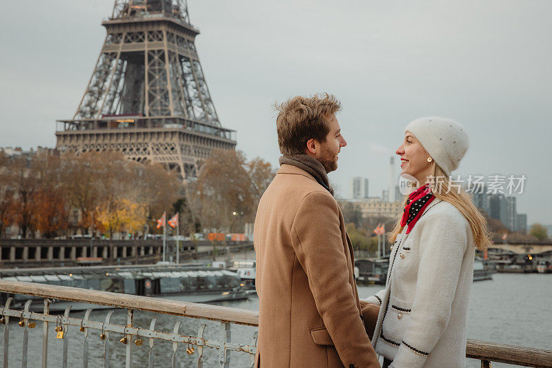 法国巴黎，一对情侣站在艾菲尔铁塔前的塞纳河桥上调情