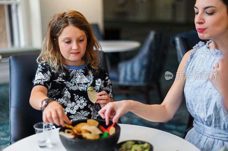 母亲和女儿在小咖啡馆或餐馆吃一碗薯片和鳄梨酱