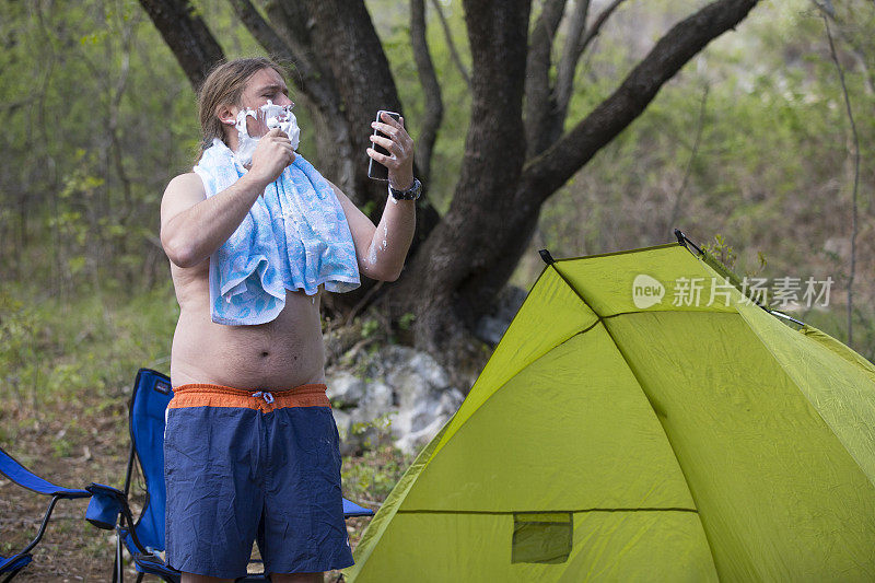 一男子在露营时剃胡子，把手机当镜子