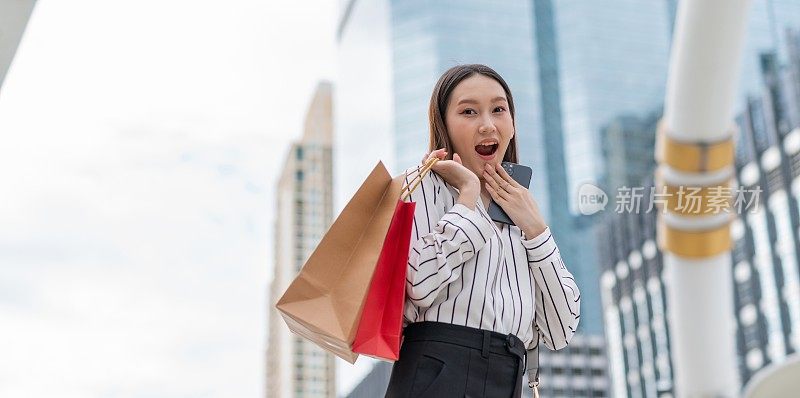 迷人聪明的亚洲女商人雇员在曼谷市中心商业区疯狂购物后，看到另一个狂欢节销售，她笑得很开心