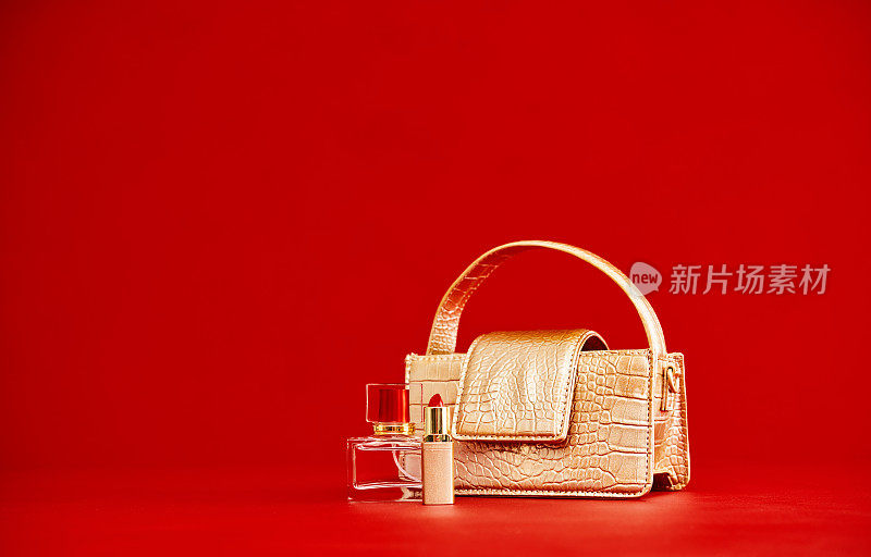 金色钱包与女性配饰香水瓶和口红。红色背景与文本复制空间