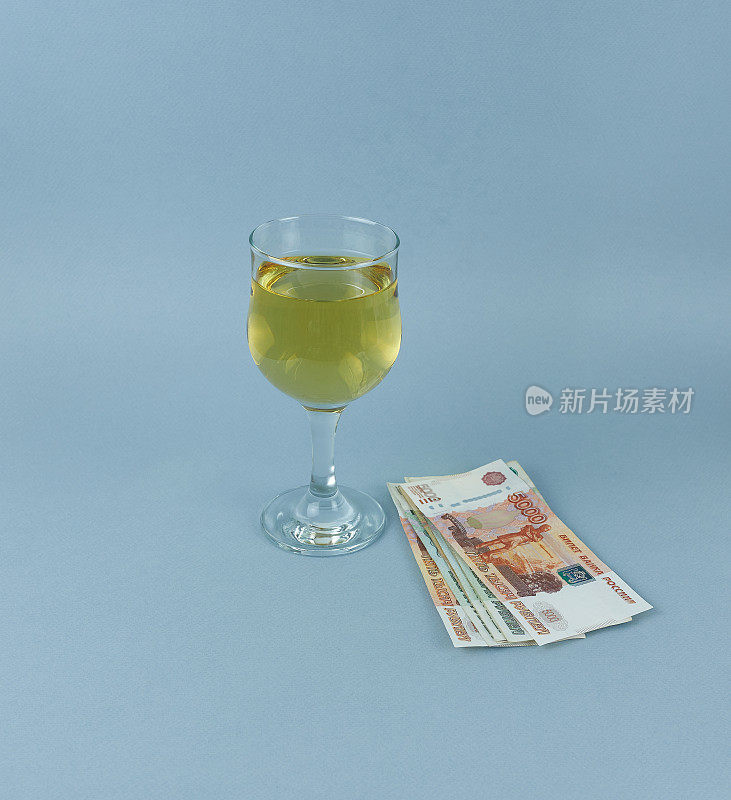 一杯白葡萄酒，蓝色背景上有500和1000卢布的钞票。概念是坏习惯，酗酒。