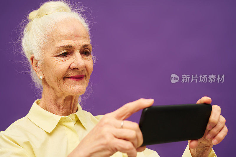 微笑的白发老妇人看着智能手机屏幕