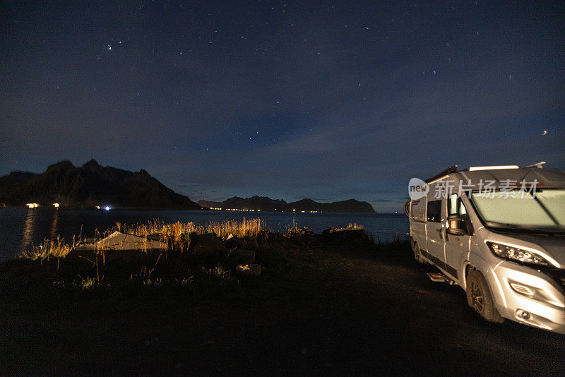 一辆露营车停在海边，星光灿烂的夜晚没有月亮。