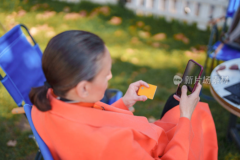 一名妇女在路边咖啡馆使用手机和信用卡