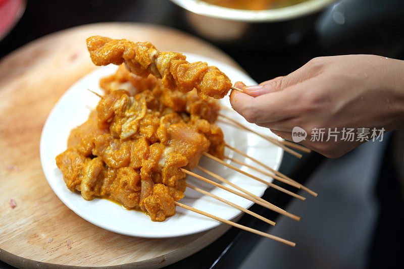 一个女人在厨房里准备沙茶，用竹签串生肉的特写镜头