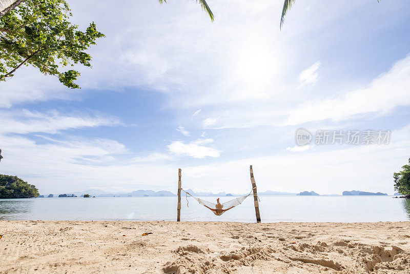 日出时，一名女子在海滩边的吊床上休息