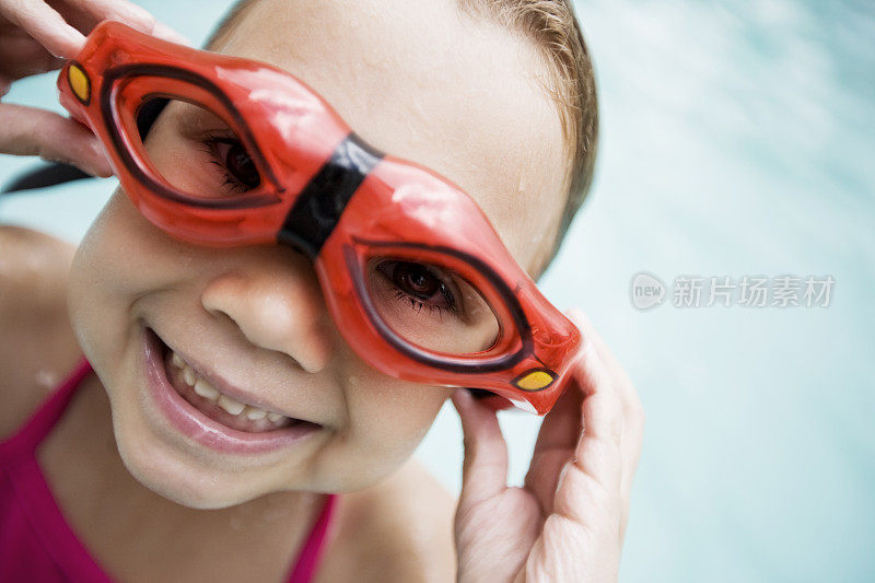 小女孩戴着护目镜在游泳池里