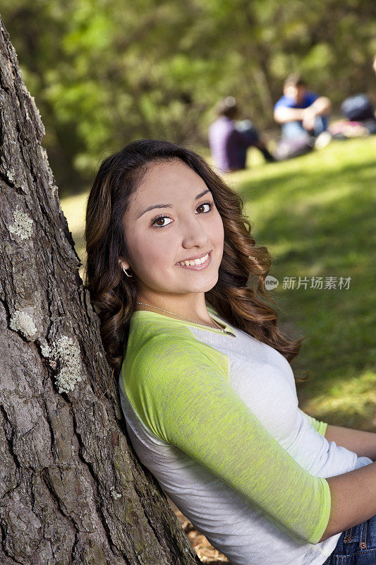 青少年:快乐的女孩在树下与朋友的背景。