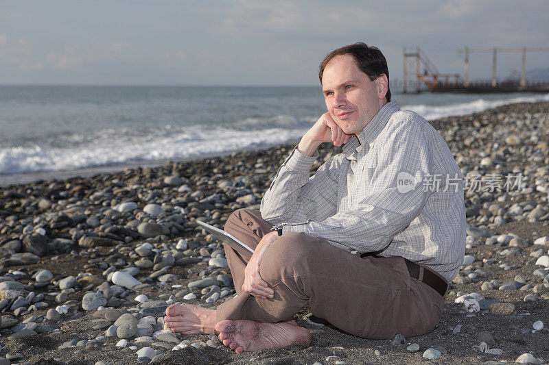 海滩上拿着笔记本电脑的男人