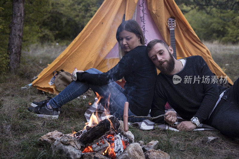 幸福的夫妇在森林里的篝火上烤香肠