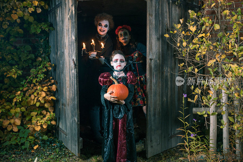 三个孩子穿着诡异的万圣节服装站在老房子前