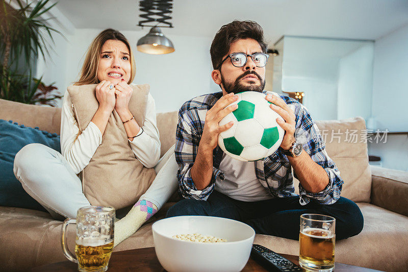 一对夫妇在家里的沙发上看足球。
