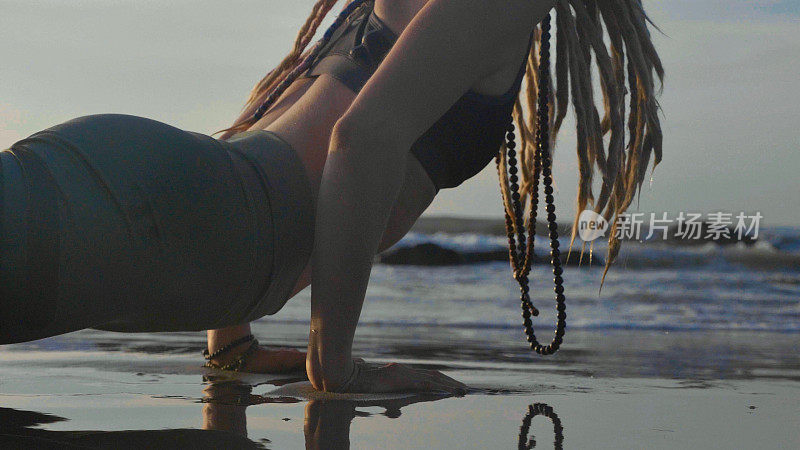日落时做瑜伽。一个年轻女人在海滩上做瑜伽运动