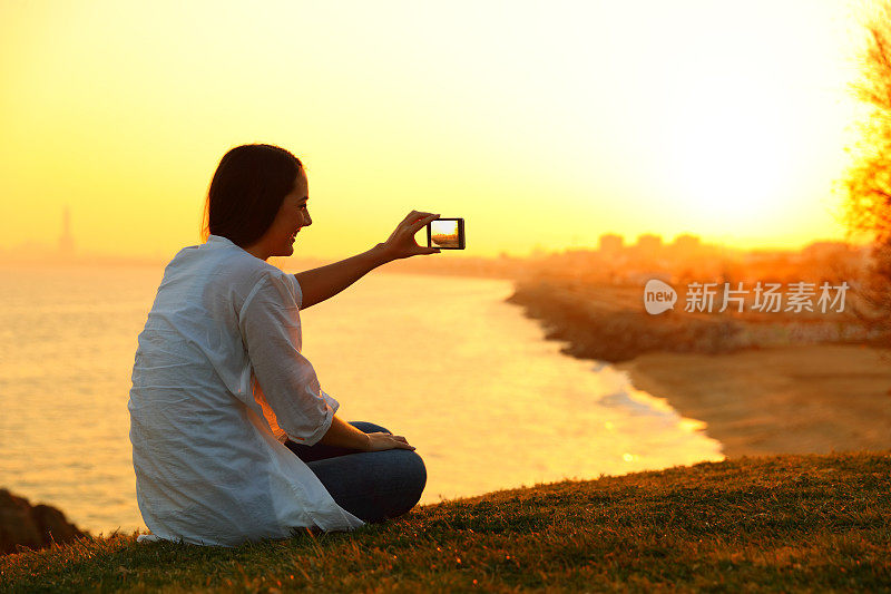 一个女人在日落时分用智能手机拍照