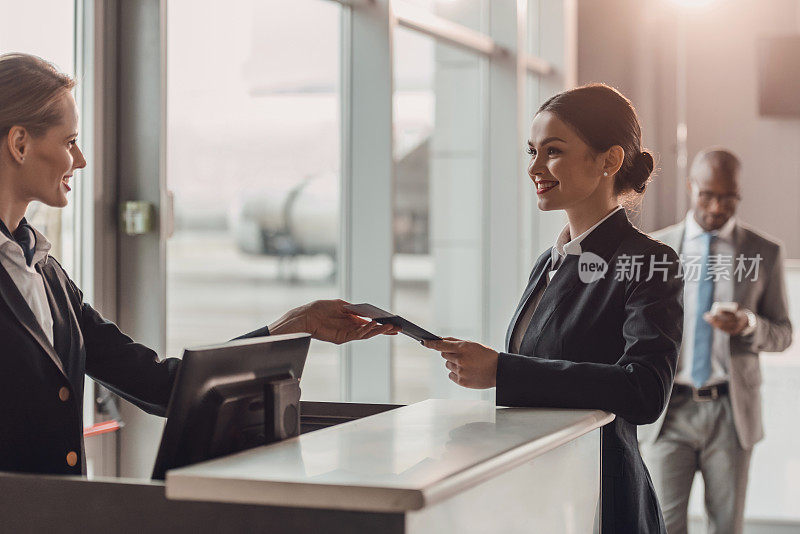 微笑的年轻女商人在机场办理登机手续时将护照和机票交给工作人员