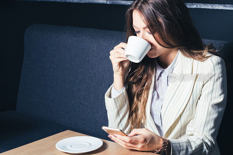 现代女孩坐在桌边喝着咖啡，用着手机。