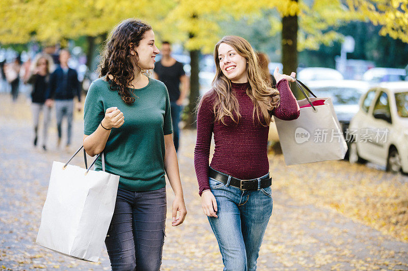 购物:两个年轻的女人拿着购物袋走在街上