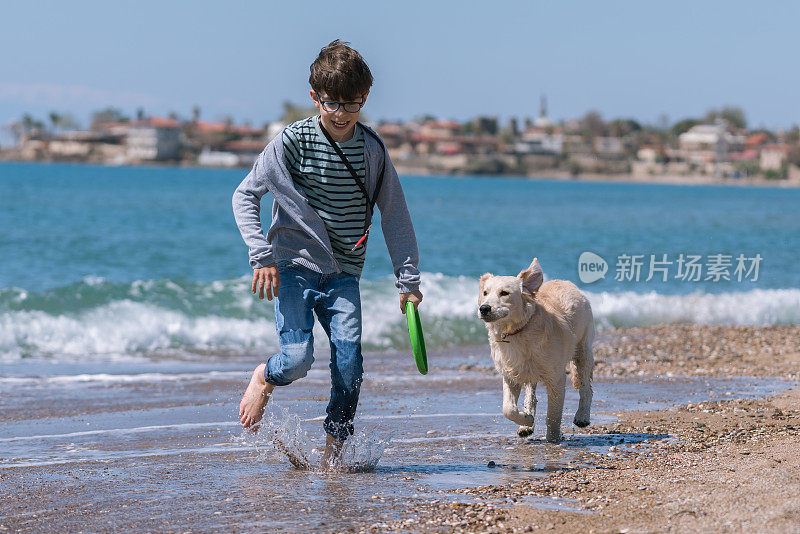快乐的男孩和她的狗在沙滩上奔跑。