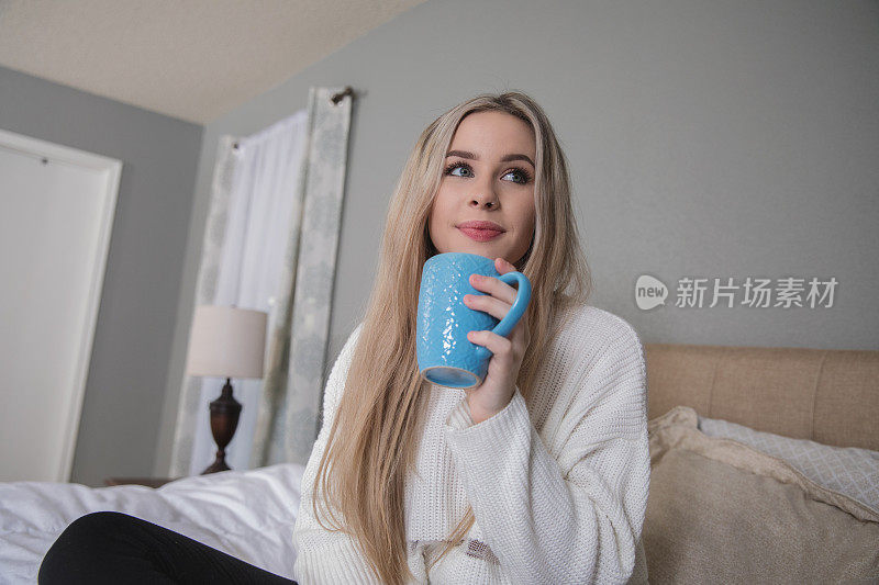 快乐的年轻女子坐在床上喝着咖啡