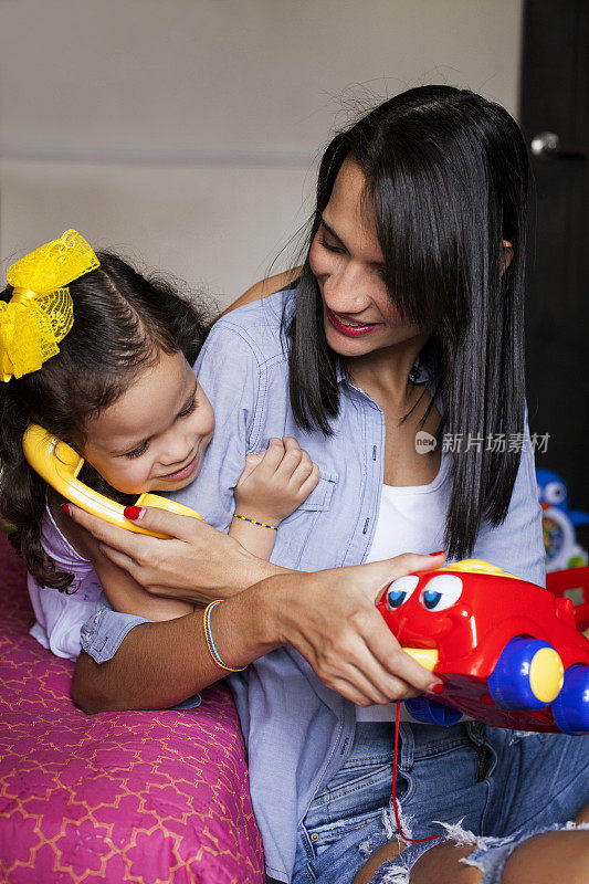 妈妈和女儿一边玩玩具手机一边微笑，享受只有妈妈和女儿的一天