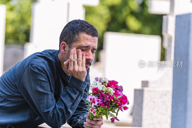 悲伤中的男性鳏夫与玫瑰花束在墓地