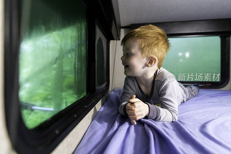 雨中的小红发男孩在野营拖车里望着窗外
