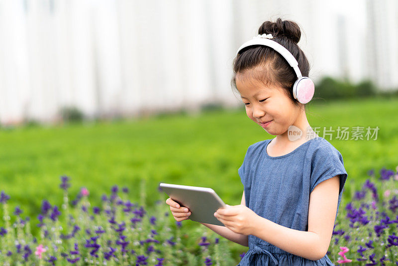 一个亚洲小女孩戴着耳机在草坪上听音乐
