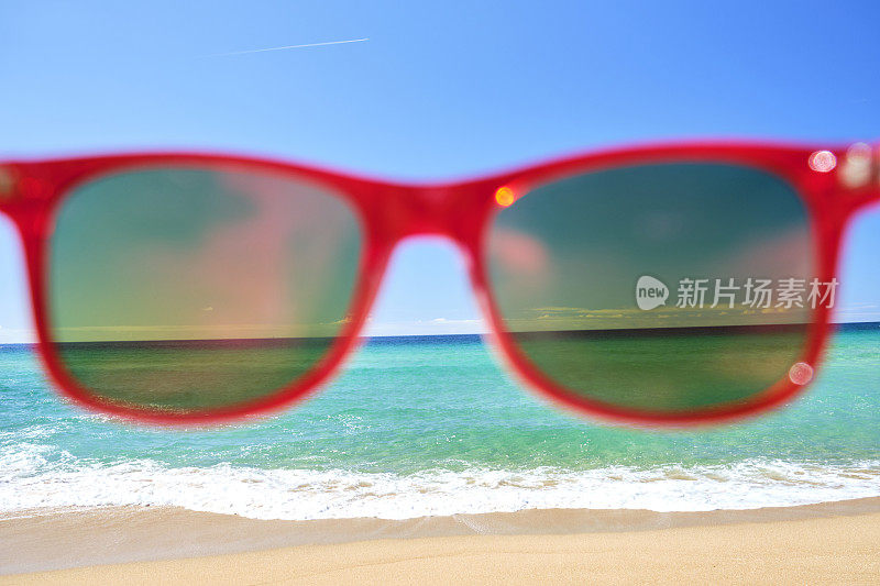 海滩度假，红色太阳镜在沙滩上与蓝天和大海。英国康沃尔。