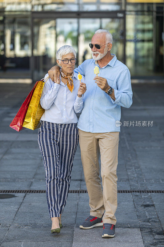 一对时尚的老夫妇在逛完购物中心后正在城市的街道上吃冰淇淋