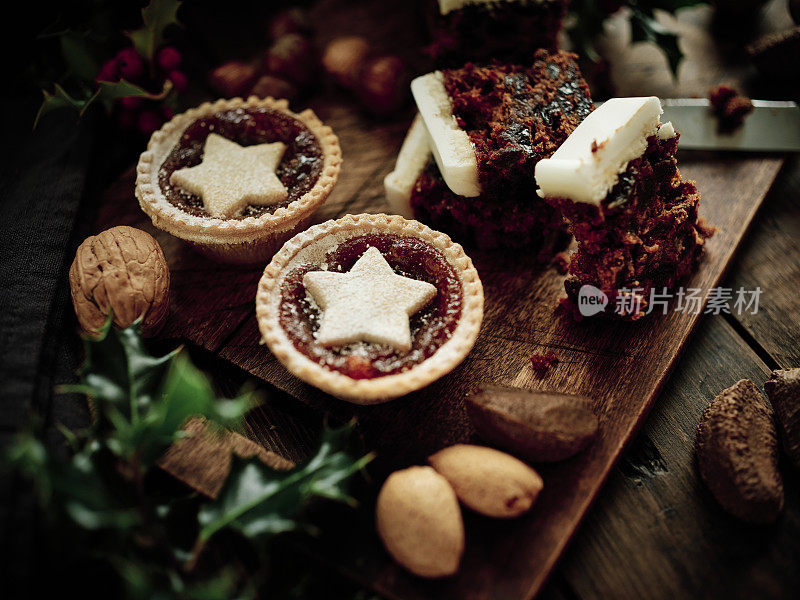 圣诞食品，肉馅饼，圣诞蛋糕，混合坚果和冬青在一个老化的深色木头表面。
