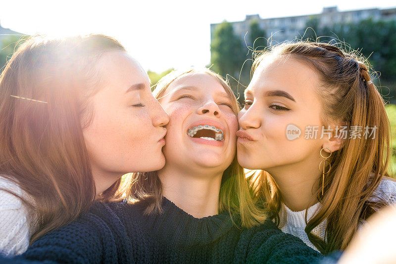 3名女生十几岁，13-15岁，在秋天的一天，在夏天的城市里，在智能手机上自拍，社交网络。开心、放松、欢笑、欢乐。牙齿的牙套。