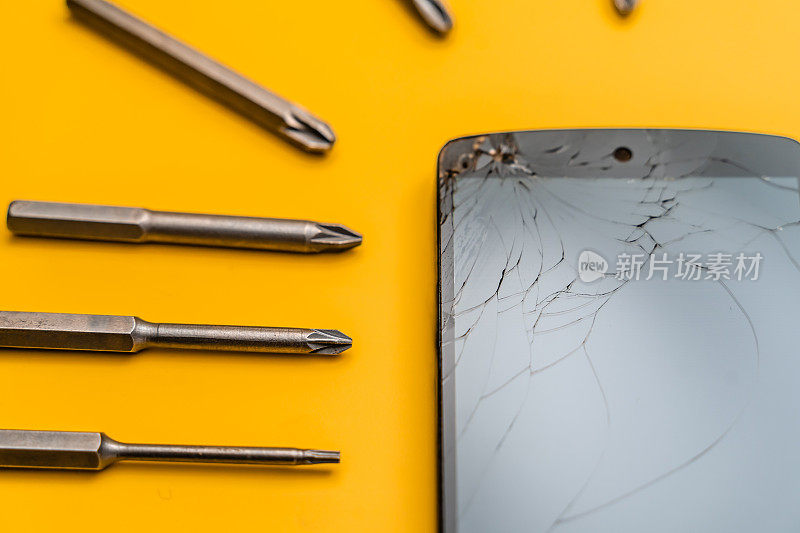 手机的特写，破碎的屏幕被钢钻头包围，黄色的背景