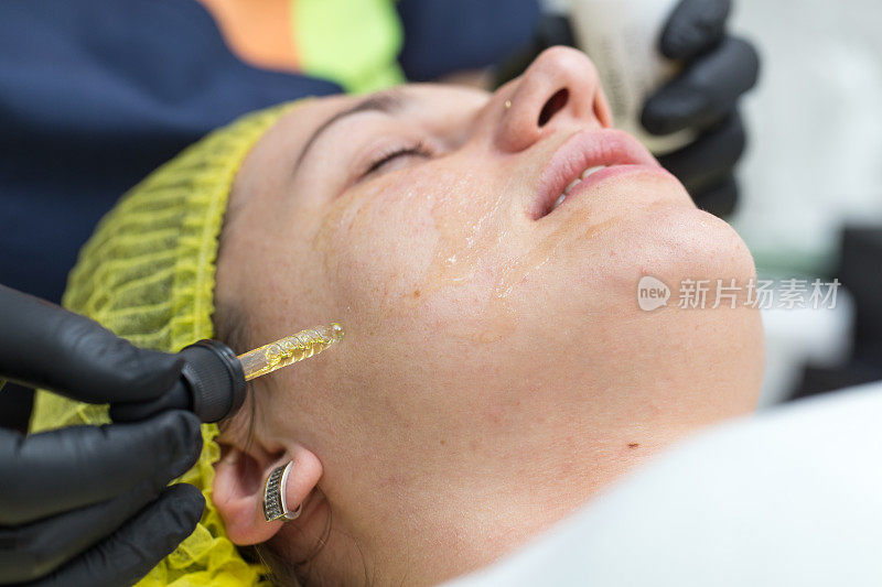 美容师用吸管将化妆品滴到女性脸上的皮肤上。