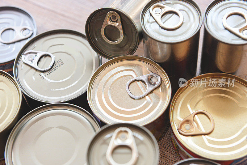 各种罐头食品在金属罐头木质的背景上，俯视图-罐头食品不易腐坏的食品储存在厨房或家庭的物品捐赠