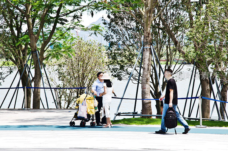 游客(包括一对夫妇和一个推着婴儿车的孩子)在中国深圳的深圳人才园漫步。这个公共主题公园与深圳湾公园和湾体育馆相连