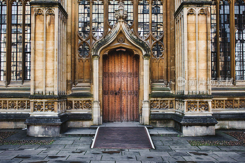 牛津神学院的外部展示了一个巨大的木门入口，柱子和彩色玻璃窗