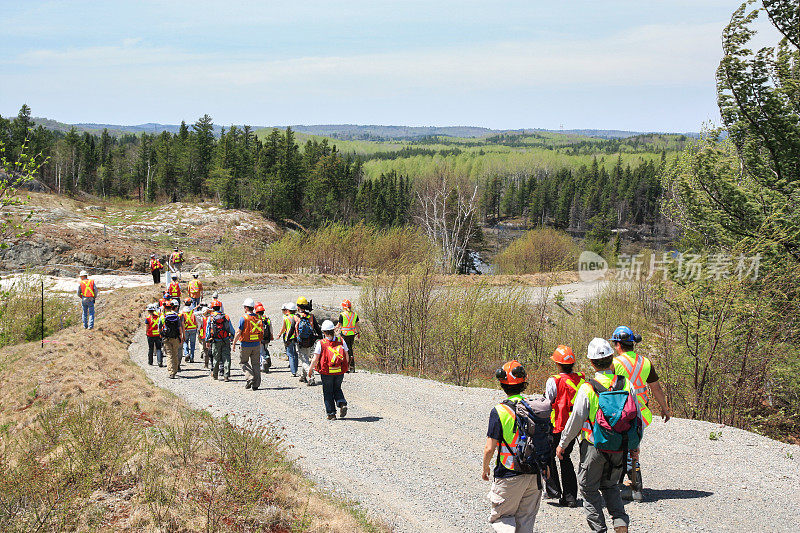 一组工人和地质学家在安全帽和高能见度背心走在道路上地质露头地点。