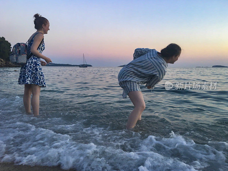 两姐妹一起在沙滩上，站在海里，擦着石头