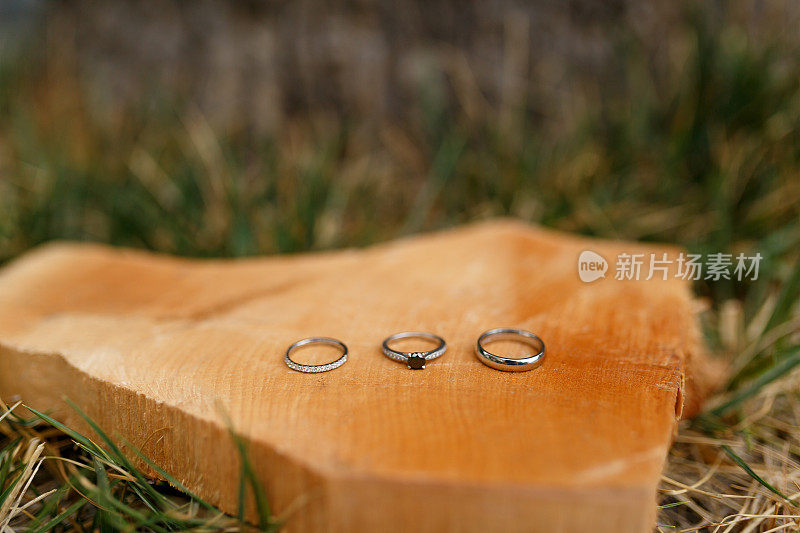 金色的结婚戒指和订婚戒指放在草地上光滑的木刻上。
