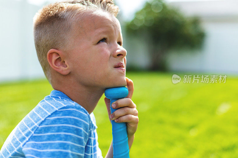 靠在塑料棒球棒上看远处的小男孩