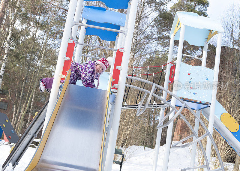 一个5岁的白人女孩正从儿童滑梯上滑下来。孩子在操场上玩得很开心。