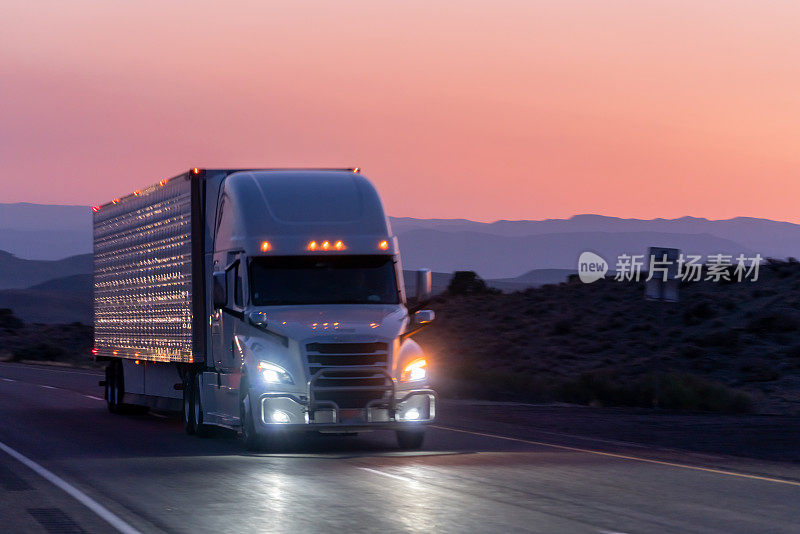 一辆商业卡车在沙漠公路上向东行驶，以交付货物，一个戏剧性的日落背景